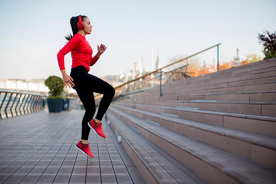 Woman wearing black and red workout clothes sprinting up steps listening to music